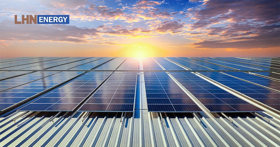 A wide view of solar panels on a rooftop under a bright sun at sunset.