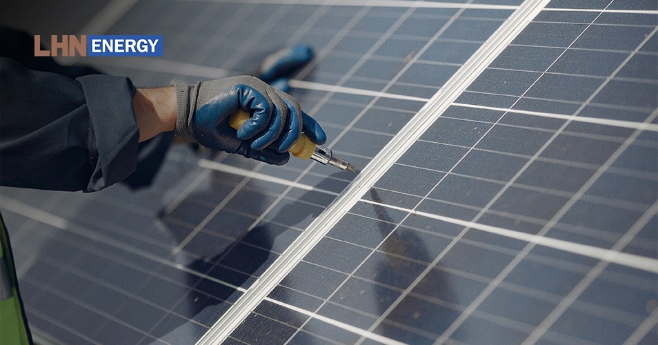 A technician wearing blue work gloves using a tool to install or repair a solar panel outdoors.