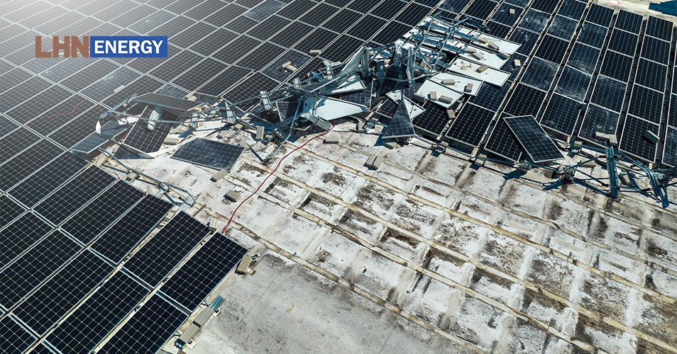 A high-angle view of a solar panel installation showing significant structural damage, with twisted metal frames and shattered panels.